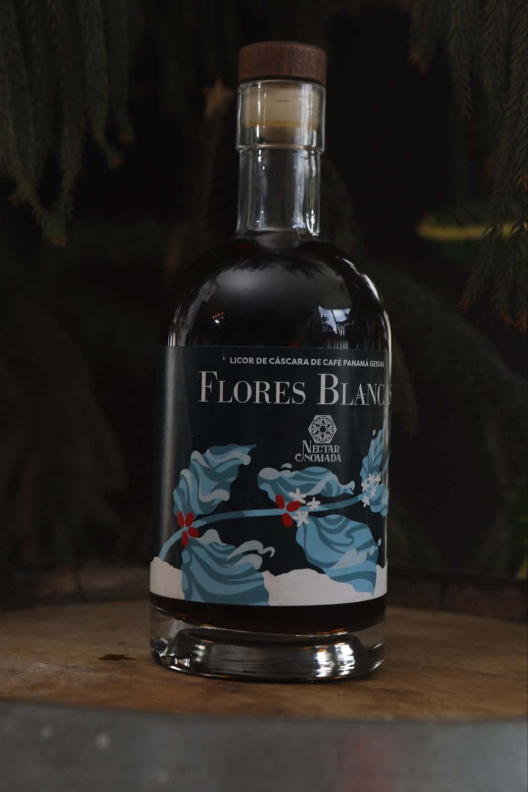 La botella sola sobre la tapa de una barrica, contra un fondo oscuro de ramas de araucaria