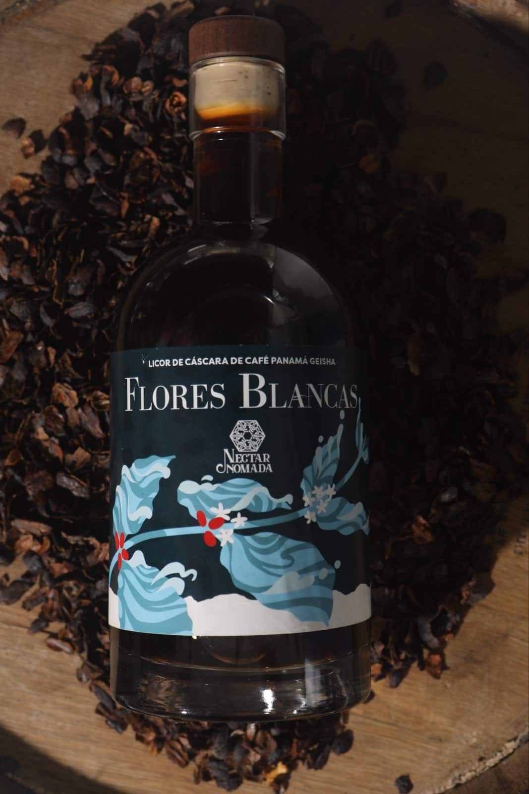 La botella de Flores Blancas rodeada de cáscara de café seca amontonada sobre la tapa de una barrica