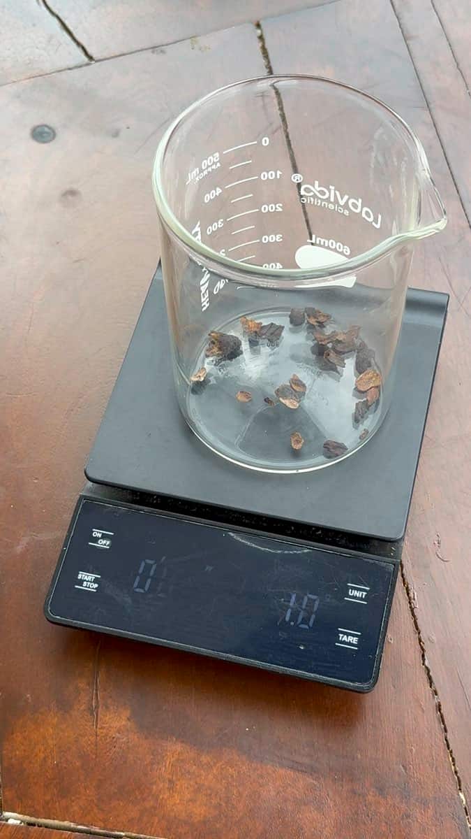 Una balanza digital sobre una mesa de madera, con un vaso de laboratorio graduado encima y trozos oscuros dentro