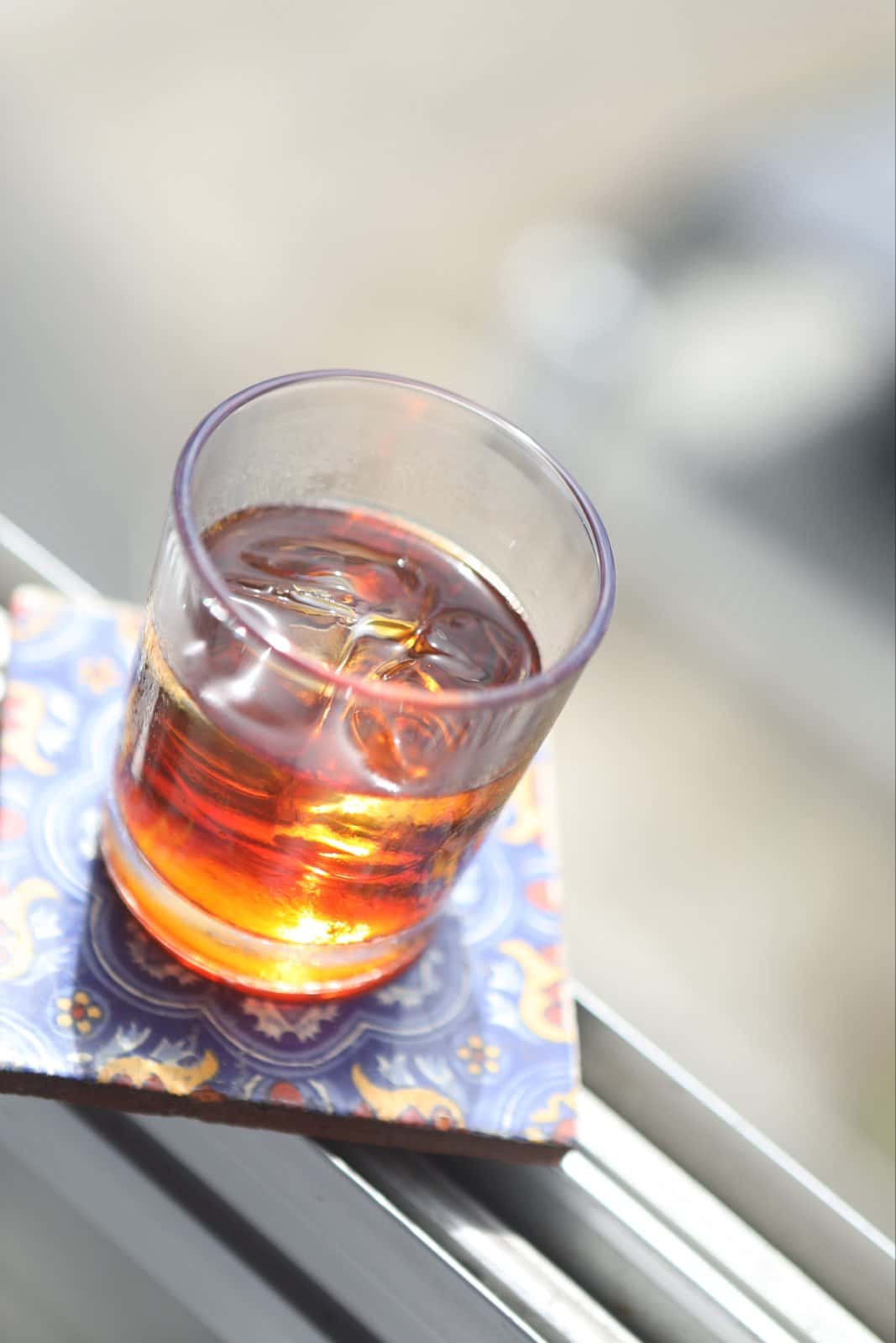 Un vaso con el licor y un hielo, sobre una baldosa pintada de azul, en la baranda de una terraza con la ciudad al fondo