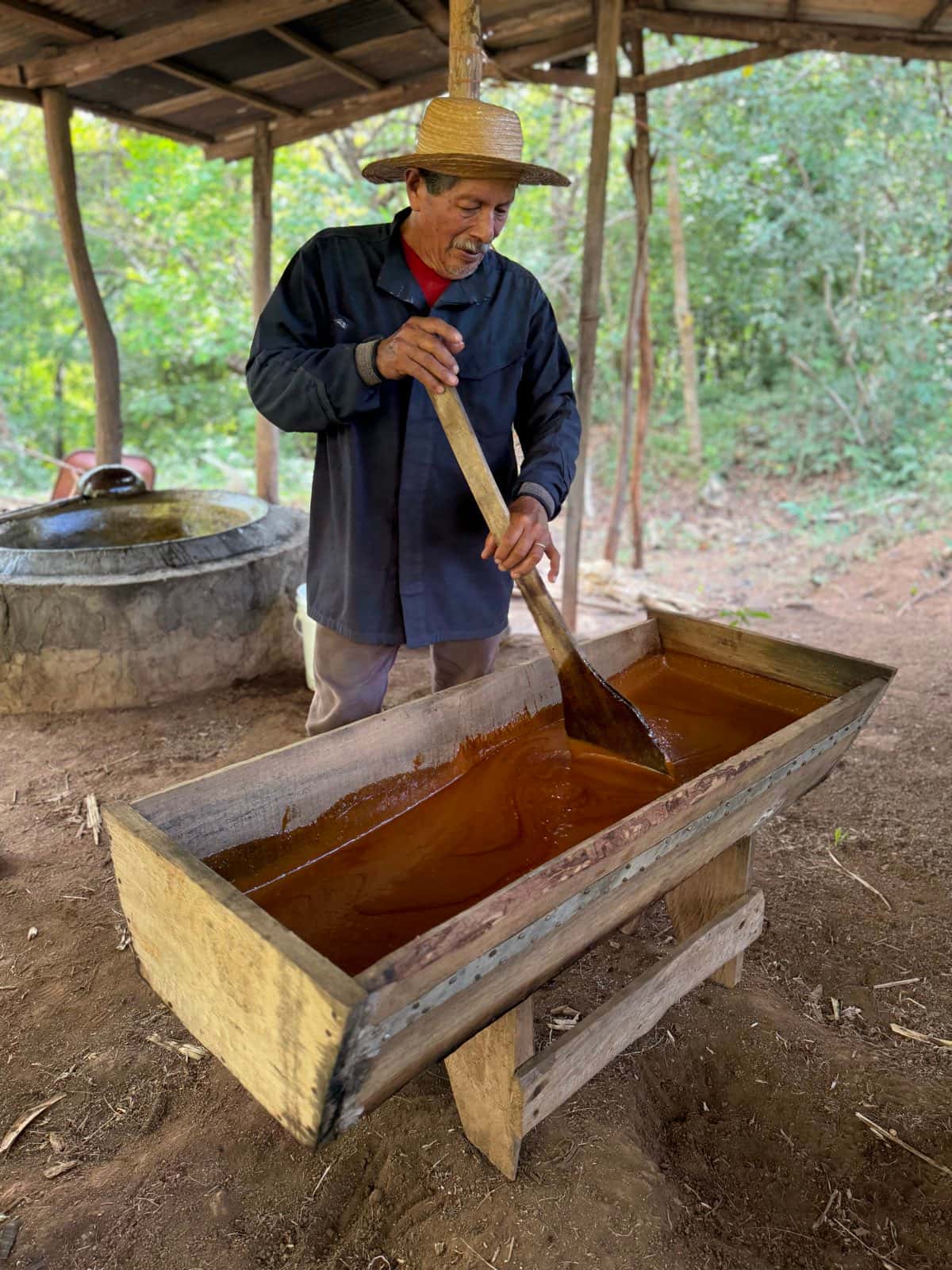 El melado, de color ámbar oscuro, trabajado con una paleta de madera dentro de una canoa larga apoyada sobre patas